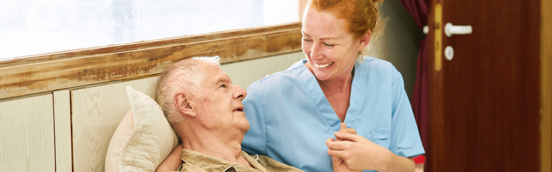 caregiver holding the hands of an elderly lying in bed